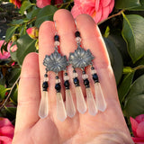 Decorative earrings with floral designs held in a hand against a floral background