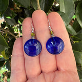 Blue earrings held in a hand with a green leafy background