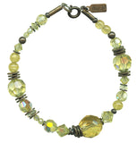 A jonquil yellow bracelet with a mix of glass and crystal beads, and metal antiquing on a bracelet with a loop at the top.